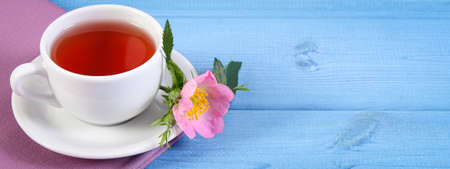 Cup of hot tea with wild rose and blooming flowers on blue boards, copy space for text or inscriptionの写真素材