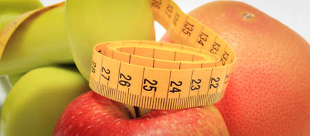 Tape measure, fresh ripe fruits and dumbbells using in fitness. Slimming, healthy nutrition and sporty lifestylesの写真素材