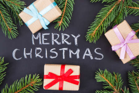 Inscription Merry Christmas, wrapped gifts with ribbon and green spruce branches on black background. Decoration for christmas timeの写真素材