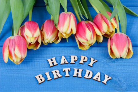 Inscription happy birthday and bouquet of fresh tulips on blue boards. Surprise for birthday occasionの写真素材