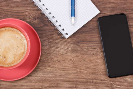 Mobile phone, cup of coffee with milk and notepad for writing notes. Copy space for text or inscriptionの写真素材