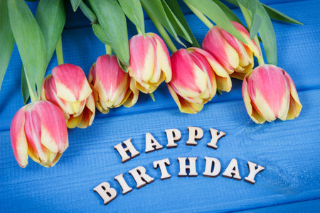 Inscription happy birthday and fresh tulips on blue boards. Surprise for birthday occasionの写真素材