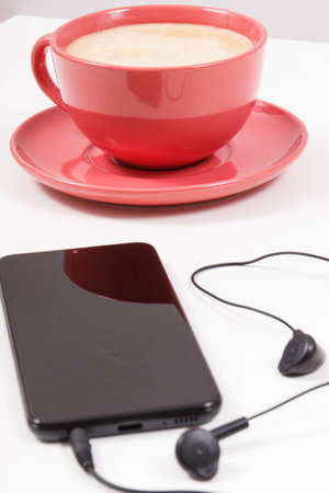 Smartphone with connected headphones and cup of coffee with milk. Relaxation time with music. White backgroundの写真素材