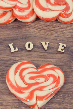 Inscription love and colorful sweet funny lollipop in shape of heart on rustic board. Surprise for birthday, valentine or other different occasionsの写真素材