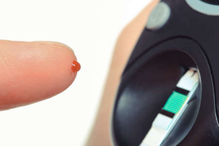 Finger with blood and glucometer. Checking and measuring sugar level. Taking blood sample from...