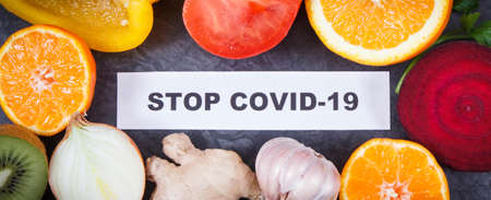 Inscription stop covid-19 and fresh ripe healthy fruits with vegetables containing natural vitamins. Immune boosting in times of Covid-19の写真素材