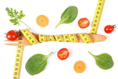 Wooden fork wrapped in centimeter and fresh vegetables on white background, concept of slimming and healthy nutritionの写真素材