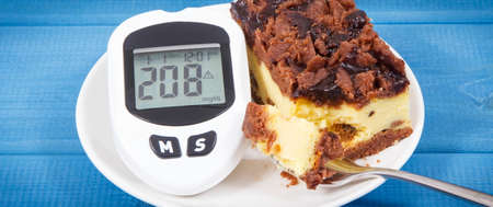 Glucose meter with high and bad result of measurement sugar level and fresh baked homemade cheesecake. Dieting during diabetesの写真素材