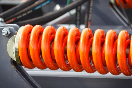 Hard orange spring made of steel. Part and detail of industrial or agricultural machine. Technologyの写真素材