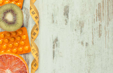 Fresh natural fruits containing vitamins, tape measure and medical pills. Choice between healthy nutrition and supplements. Copy space for text or inscriptionの写真素材