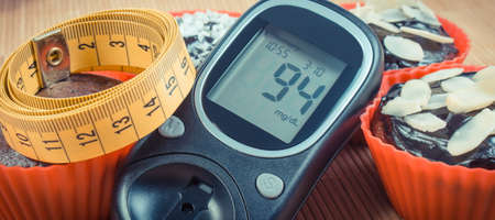 Glucose meter for checking and measuring sugar level, fresh baked chocolate muffins and tape measure. Diabetes, slimming and dessert for different occasionsの写真素材
