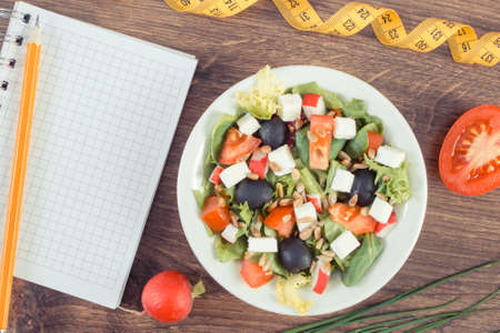 Fresh prepared greek salad with feta cheese and notepad with tape measure. Slimming and healthy nutritionの写真素材