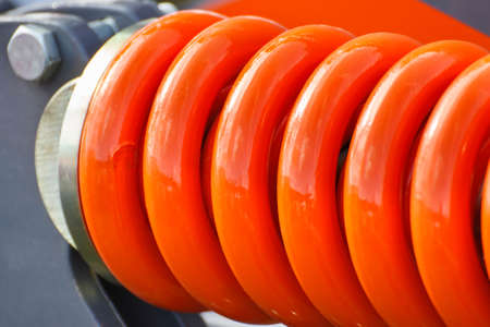 Big and hard orange steel spring as part and detail of industrial or agricultural machine. Technologyの写真素材