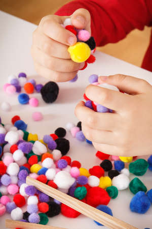 Preschooler playing with small colorful pompoms. Development of kids motor skills, coordination, creativity and logical thinkingの写真素材