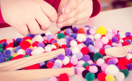 Little baby boy playing with small fluffy colorful pompoms. Development of kids motor skills, coordination, creativity and logical thinkingの写真素材