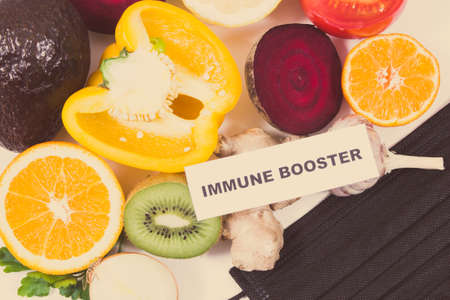 Inscription immune booster, fresh ripe fruits with vegetables and protective mask. Source natural healthy vitamins and minerals. Beneficial eating in times of Covid-19の写真素材