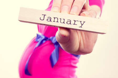 Pregnant woman in pink dress with blue ribbon showing word january written on wooden cube. Expecting for newborn and expansion of familyの写真素材