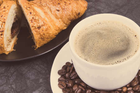 White glass cup of coffee and fresh baked croissant with chocolate. Vintage photoの写真素材