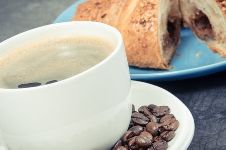 Breakfast consisting of fresh baked croissant with chocolate and coffee in glass cupの写真素材