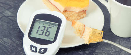 Glucose meter for checking and measuring sugar level, creamy sweet sponge cake with jelly and cup of coffee. Nutrition during diabetes. Festive dessertの写真素材