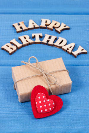 Inscription happy birthday and wrapped gift with ribbon and red heart on blue boardsの写真素材