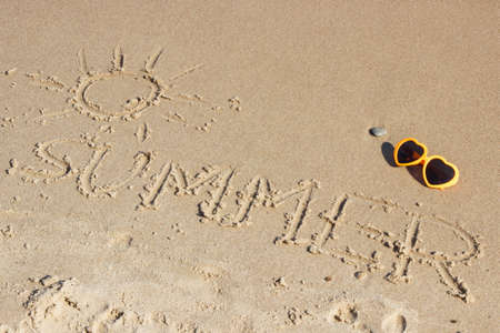 Inscription summer with shape of sun and sunglasses on sand at beach. Concept of vacation timeの写真素材