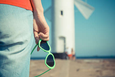 Woman with sunglasses in shape of heart on west breakwater. Windmill Stawa Mlyny in Swinoujscie in background. Summer and vacation timeの写真素材