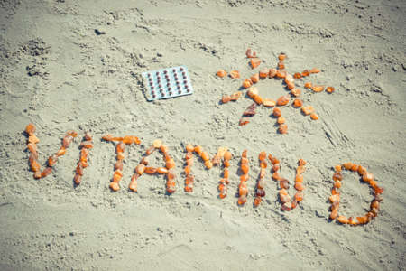 Medical pills, inscription vitamin D and shape of sun made of amber stones on sand at beach, concept of vacation time and prevention of vitamin D deficiencyの写真素材