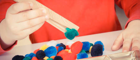 Preschooler playing with small colorful pompoms and wooden tongs. Development of kids motor skills,...