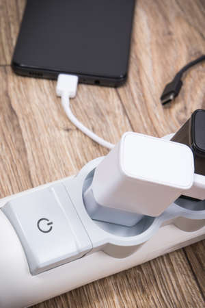 Smartphone, mobile phone and chargers connected to electrical power strip. Various devices charging...