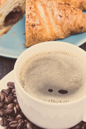 White glass cup of coffee and fresh baked croissant with chocolate on blue plate for breakfastの写真素材