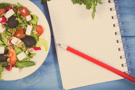 Fresh prepared greek salad with feta cheese and notepad for writing notes. Healthy nutritionの写真素材