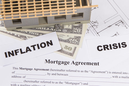 Small toy house under construction, mortgage agreement form, dollar bills and inscriptions inflation and crisis. High prices of real estate and financing purchase or construction of houseの写真素材