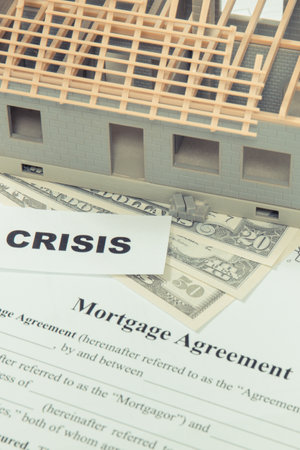 Unfinished small toy house, mortgage agreement form, dollar bills and inscription crisis. High...