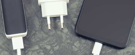 Black smartphone with connected white plug of external powerbank. Mobile phone charging