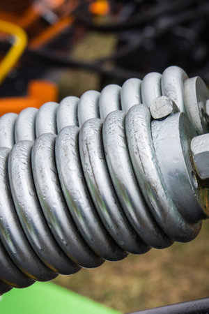 Silver hard spring made of steel. Detail and part of big industrial or agricultural machine. Technologyの写真素材