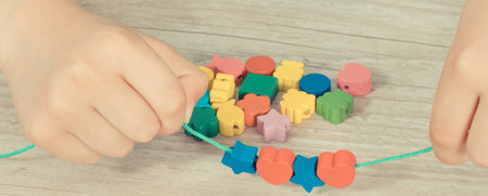 Hands of little kid making bracelet from thread and colored beads. Development of children motor skills, coordination, creativity and logical thinkingの写真素材