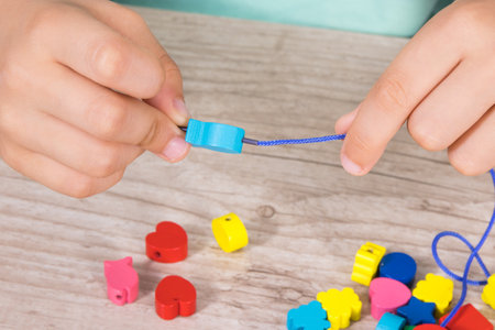 Hands of little kid making bracelet from thread and colored beads. Development of children motor...
