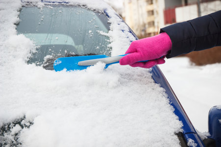Hand of woman using brush and remove snow from car and windscreen. Winter problems in transportationの写真素材