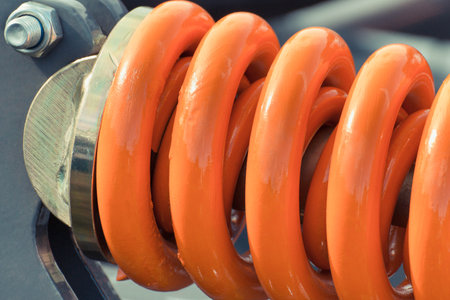 Hard orange spring made of steel. Part of big industrial or agricultural machine. Technologyの写真素材