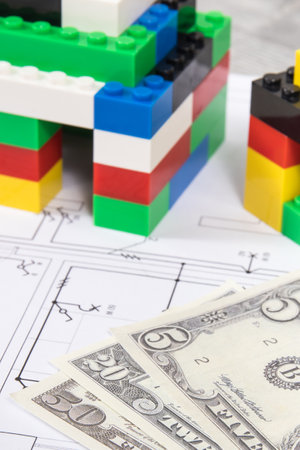 Small houses made of colorful toy blocks, electrical diagrams of house and dollar banknotes. Subject of building home costsの写真素材