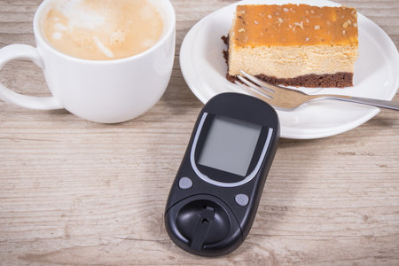 Glucometer for measuring and checking sugar level, piece of fresh baked sweet cheesecake and cup of...