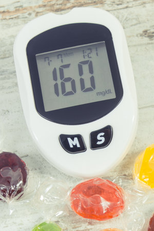 Glucometer with high result of sugar level and colorful candies. Healthy lifestyle, nutrition and...