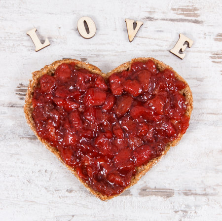 Fresh baked wholegrain bread in shape of heart with strawberry jam and inscription love. Old rustic backgroundの写真素材