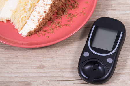 Glucometer and portion of sweet cake with chocolate. Measuring and checking sugar level during diabetesの写真素材