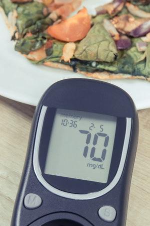 Glucose meter using for sugar level control and piece of fresh baked vegetarian pizza. Nutrition and...