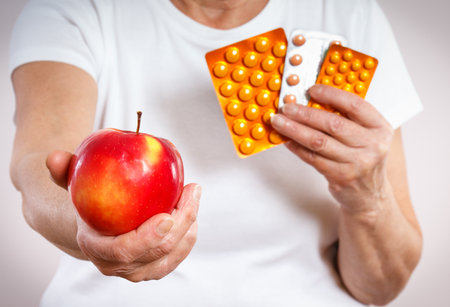 Senior woman with tablets, vitamins or supplements and fresh apple in hand. Choice between eating fruits and taking supplements for strengthening immunity in old ageの写真素材