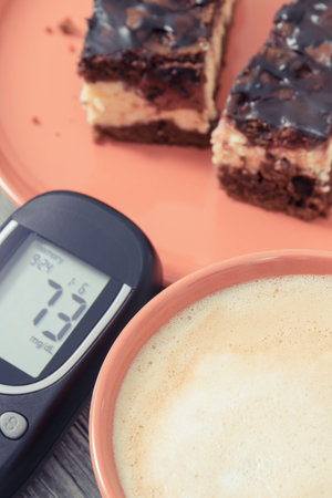Glucometer for measuring sugar level, pieces of fresh baked cheesecake with cherries and chocolate, cup of coffee with milk. Nutrition during diabetes conceptの写真素材