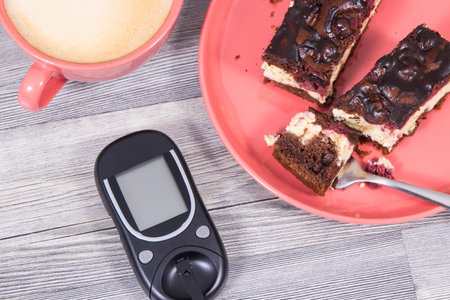 Glucometer using for measuring sugar level, pieces of fresh baked cheesecake with cherries and chocolate, cup of coffee with milk. Nutrition during diabetes conceptの写真素材