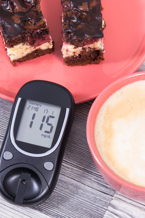 Glucometer with result of measurement sugar level, pieces of cheesecake with cherries and chocolate, cup of coffee with milk. Nutrition during diabetes conceptの写真素材